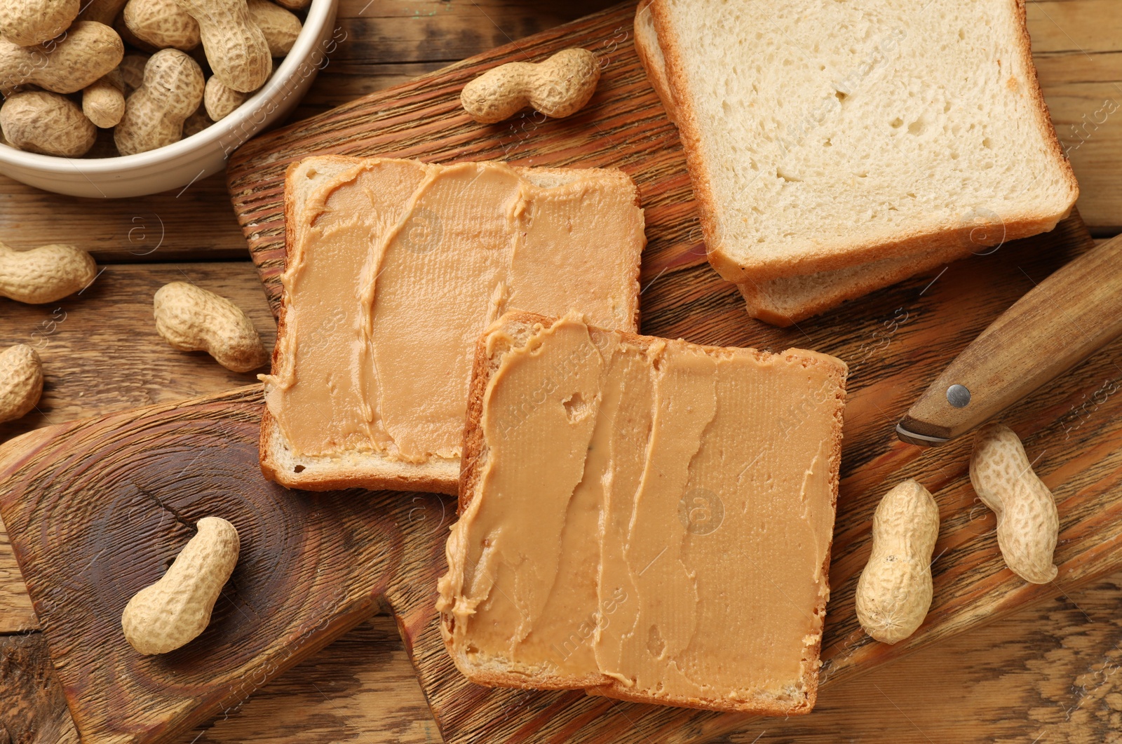 Photo of Tasty peanut butter sandwiches and peanuts on wooden table, flat lay