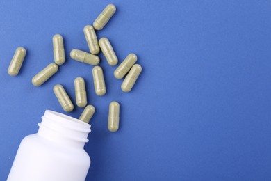 Photo of Bottle and vitamin capsules on blue background, top view. Space for text