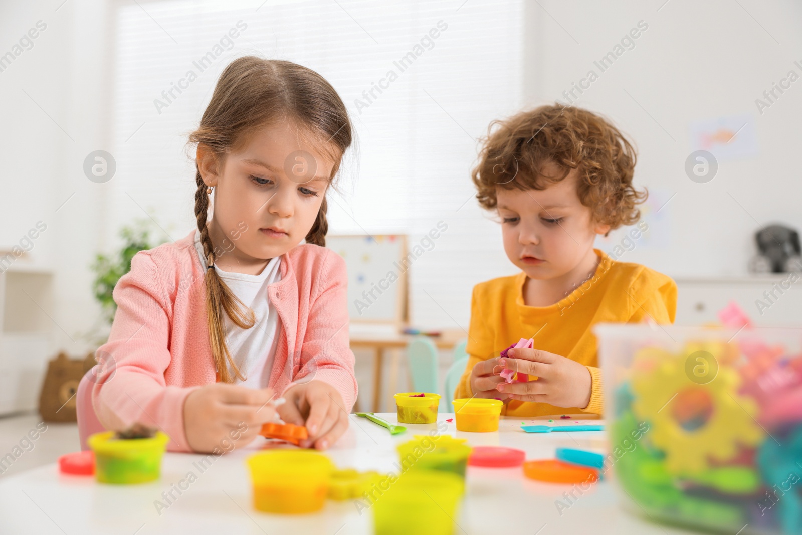 Photo of Cute little children modeling from plasticine at white table in kindergarten