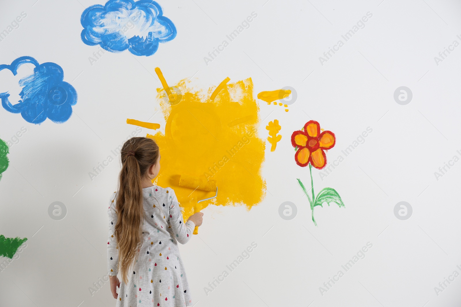 Photo of Little child painting wall with roller brush indoors