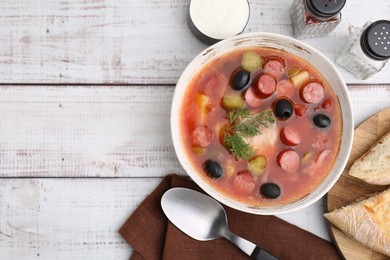 Photo of Meat solyanka soup with thin dry smoked sausages served on white wooden table, flat lay. Space for text