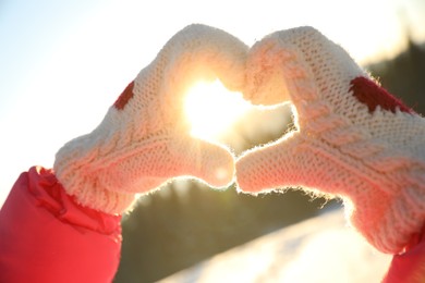 Woman making heart with hands outdoors at sunset, closeup. Winter vacation