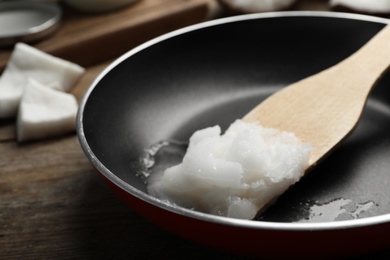 Photo of Frying pan with coconut oil and wooden spatula on wooden table, closeup. Healthy cooking