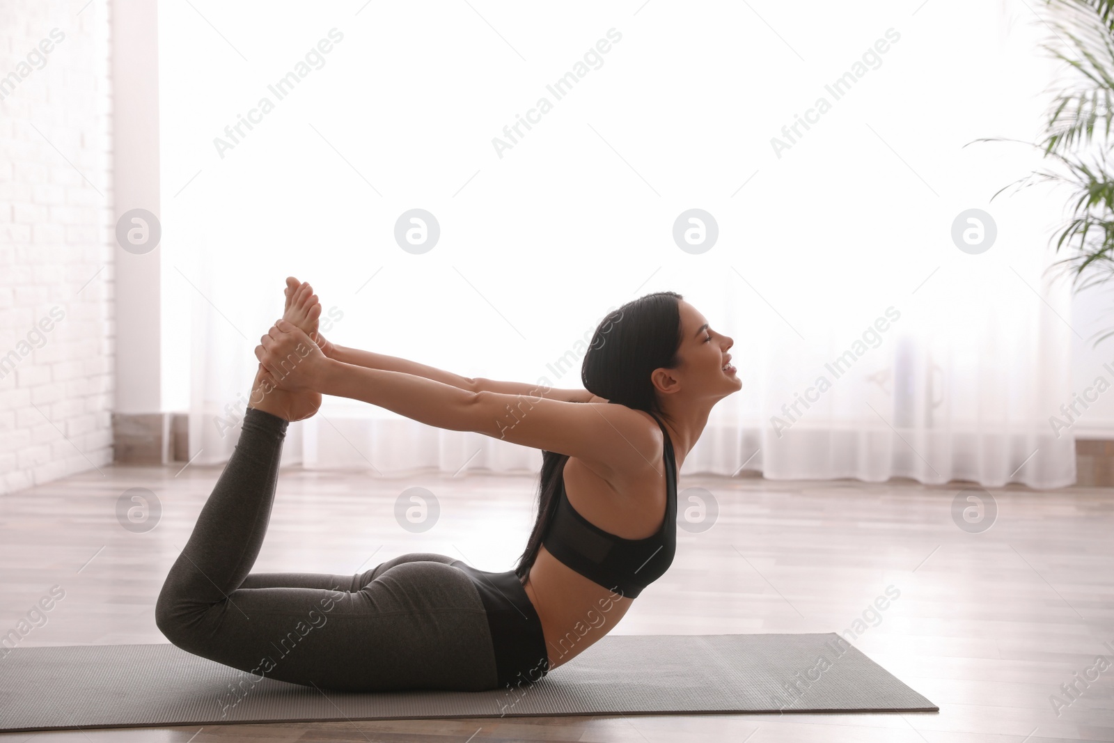 Photo of Young woman practicing bow asana in yoga studio. Dhanurasana pose