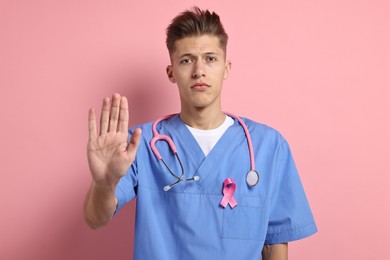 Photo of Mammologist with pink ribbon showing stop gesture on color background. Breast cancer awareness