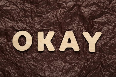Photo of Word Okay made of wooden letters on crumpled paper, top view