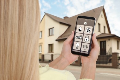 Image of Woman using smart home control system via mobile phone near house outdoors, closeup