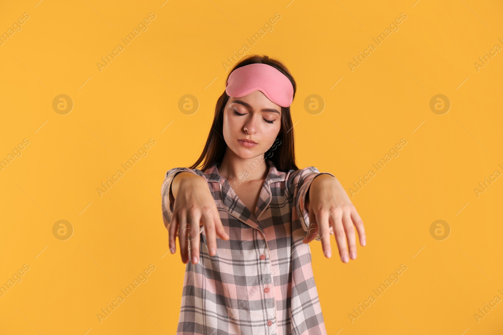 Photo of Young woman wearing pajamas and mask in sleepwalking state on yellow background