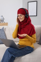 Muslim woman using video chat on laptop at couch in room