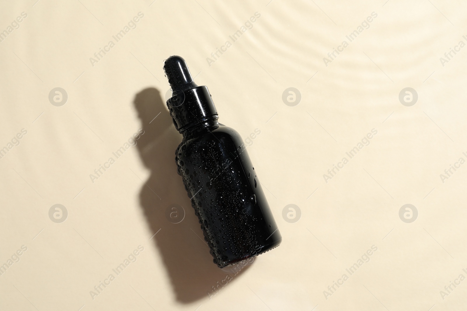 Photo of Bottle of cosmetic oil in water on beige background, top view