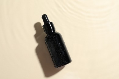 Photo of Bottle of cosmetic oil in water on beige background, top view