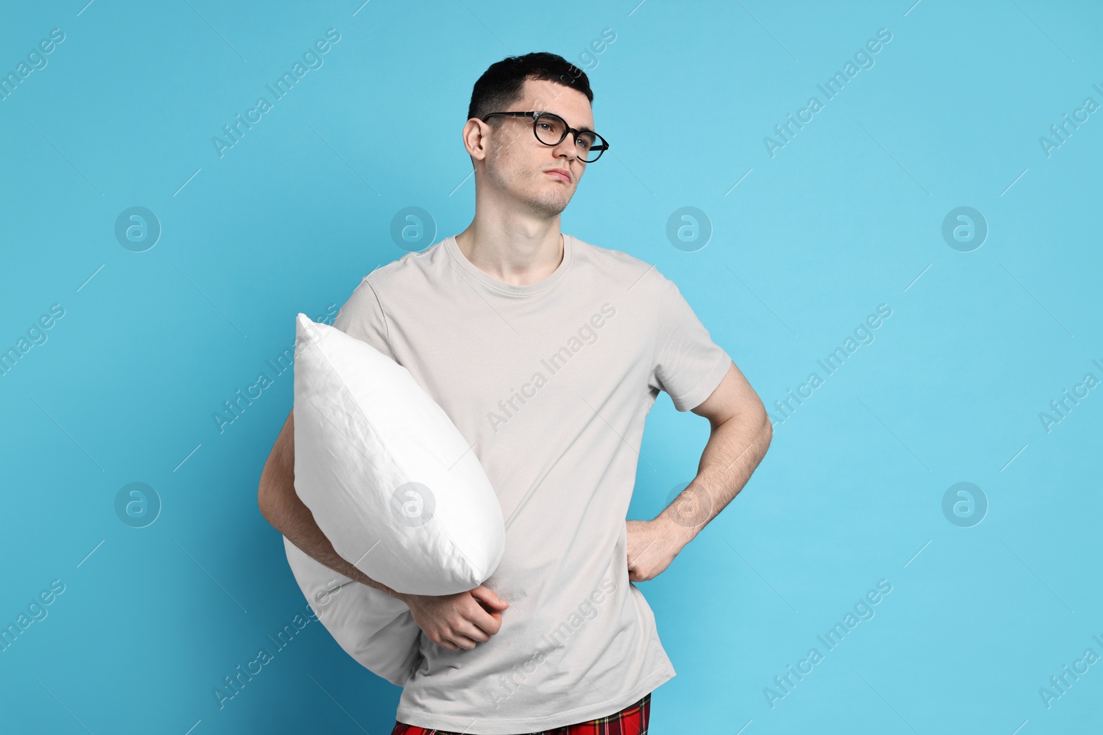 Photo of Man in pyjama holding pillow on light blue background
