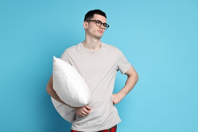 Man in pyjama holding pillow on light blue background