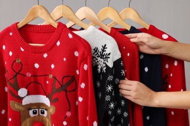 Woman choosing Christmas sweater from rack near light wall, closeup