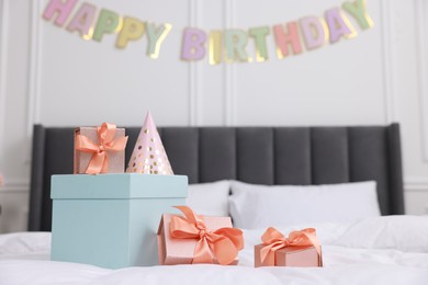 Photo of Many gift boxes and party hat on bed in room. Happy Birthday