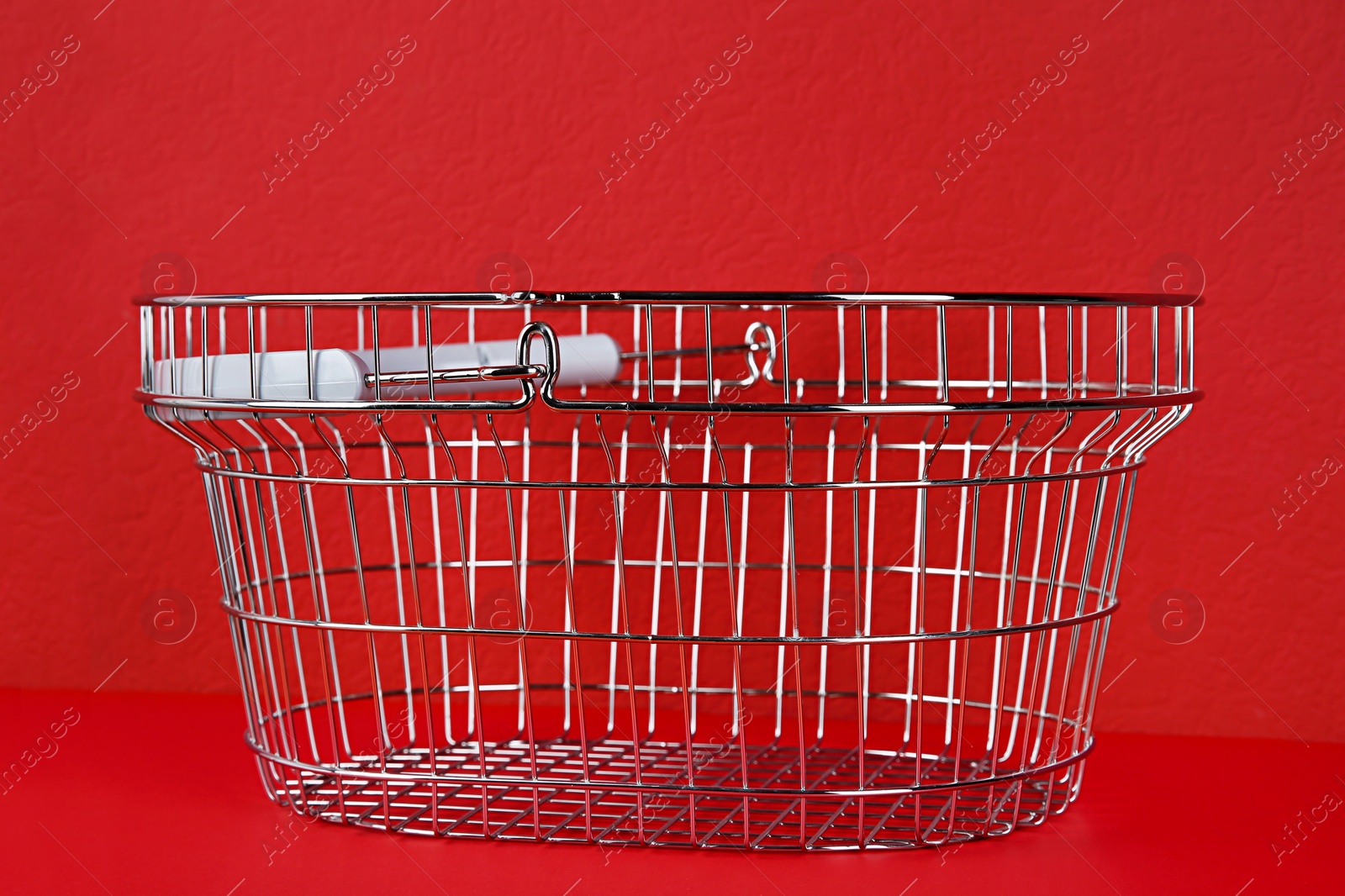 Photo of Empty metal shopping basket on red background