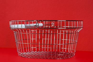 Empty metal shopping basket on red background