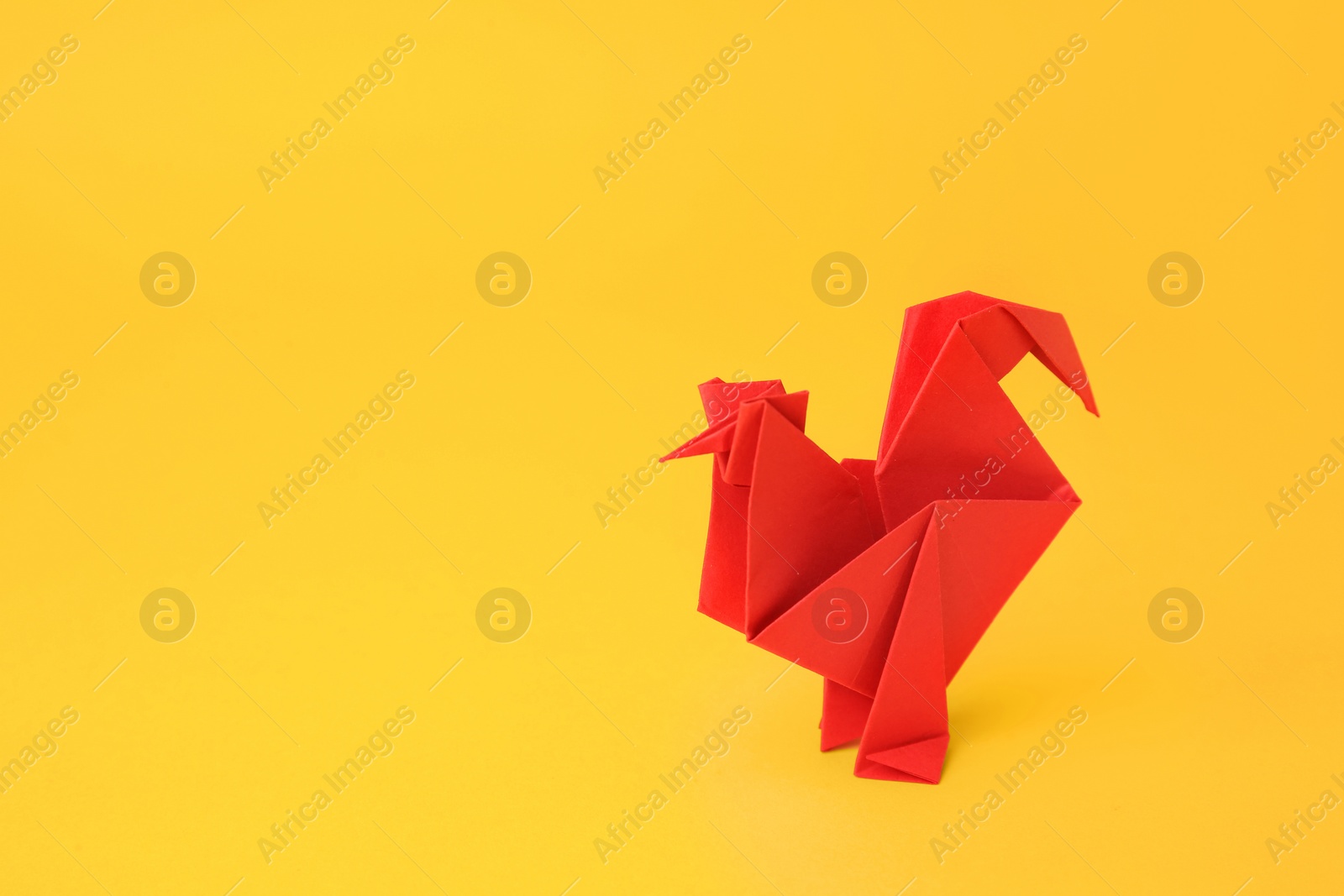 Photo of Origami art. Handmade red paper rooster on yellow background, space for text