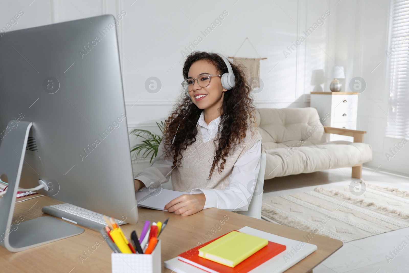 Photo of African American woman with headphones using modern computer for studying at home. Distance learning