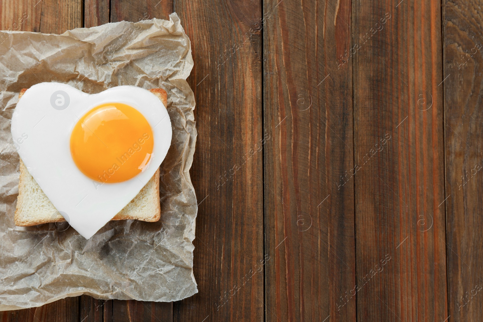 Photo of Tasty toast with heart shaped fried egg on wooden table, top view. Space for text