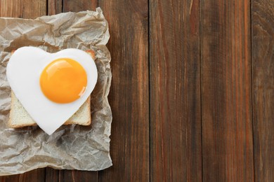 Photo of Tasty toast with heart shaped fried egg on wooden table, top view. Space for text