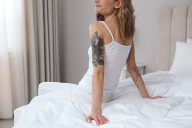 Photo of Beautiful woman with tattoos on arms in bedroom, closeup
