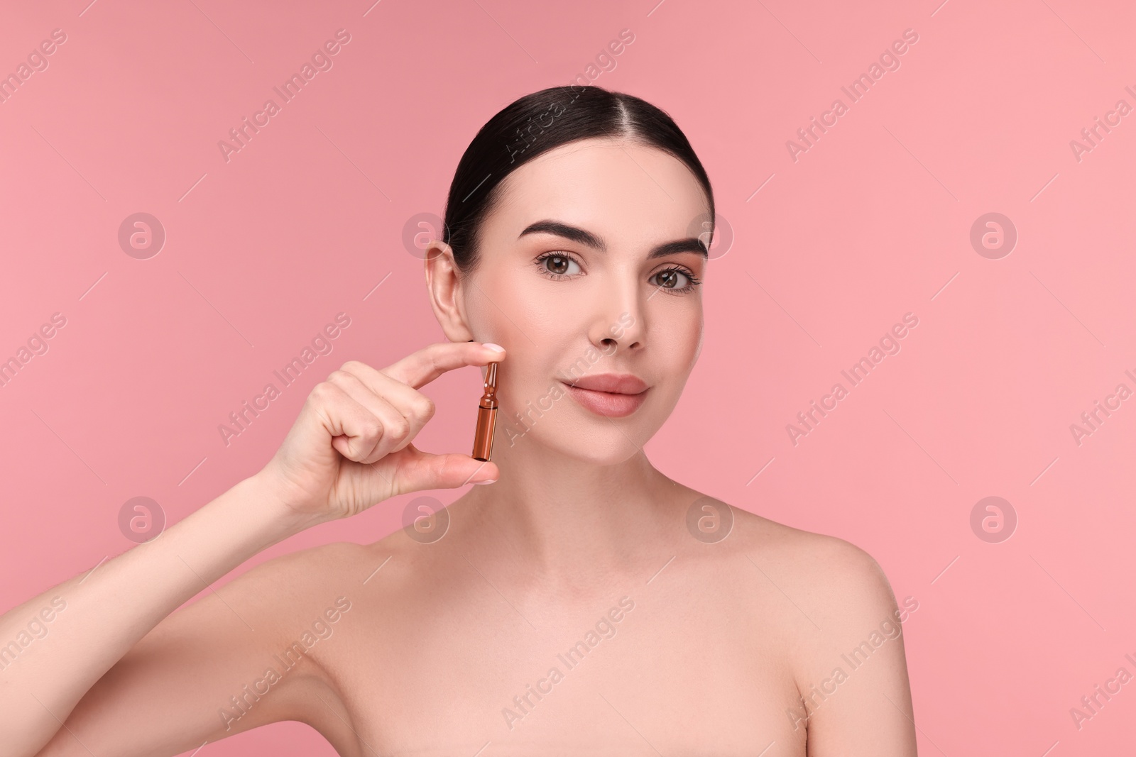 Photo of Beautiful young woman holding skincare ampoule on pink background