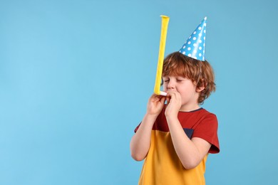 Photo of Birthday celebration. Cute little boy in party hat with blower on light blue background, space for text
