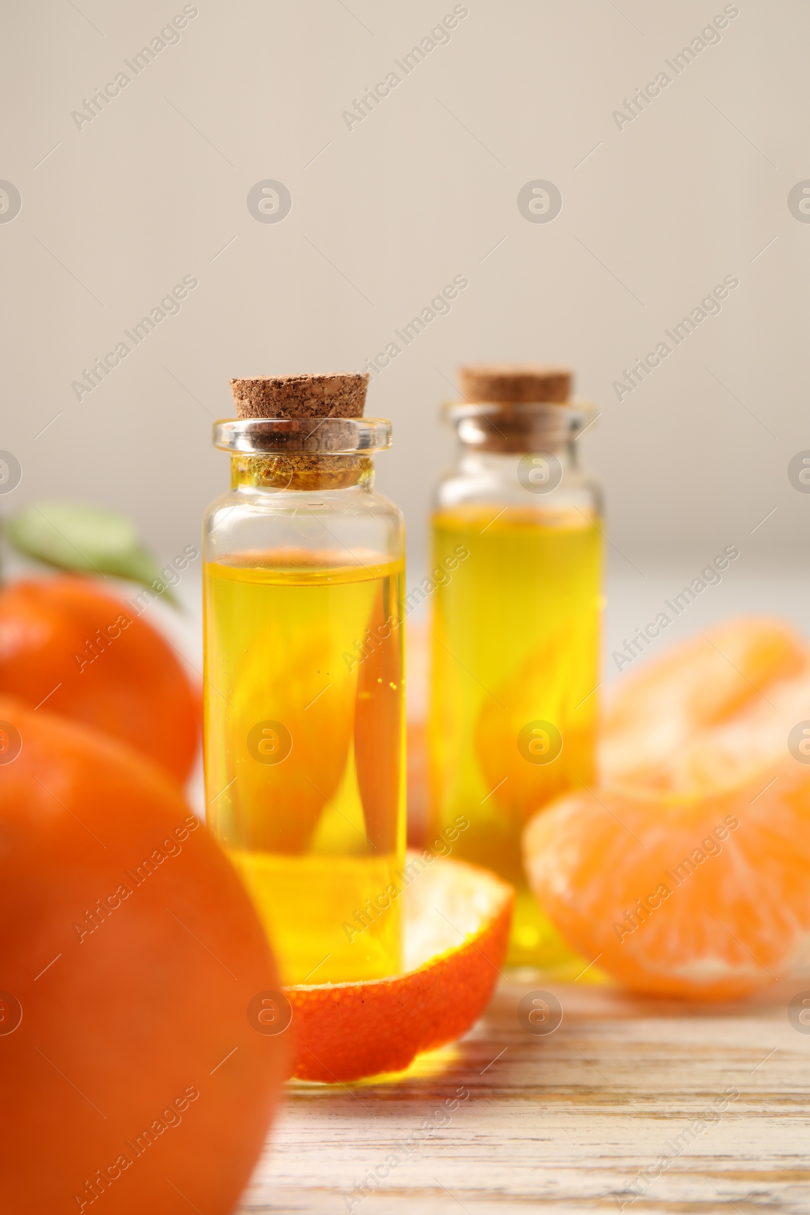 Photo of Bottles of tangerine essential oil, fresh fruits and peel on white wooden table