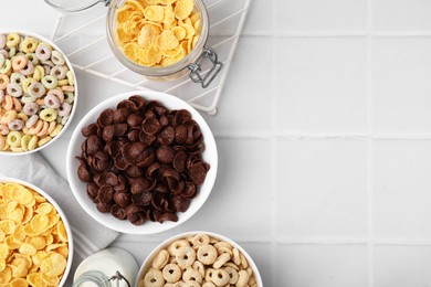 Photo of Different delicious breakfast cereals and milk on white tiled table, flat lay. Space for text