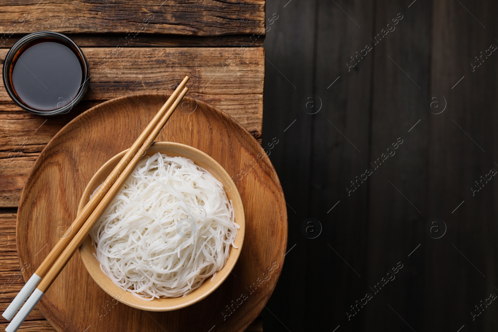 Photo of Bowl with cooked rice noodles, soy sauce and chopsticks on wooden table, flat lay. Space for text