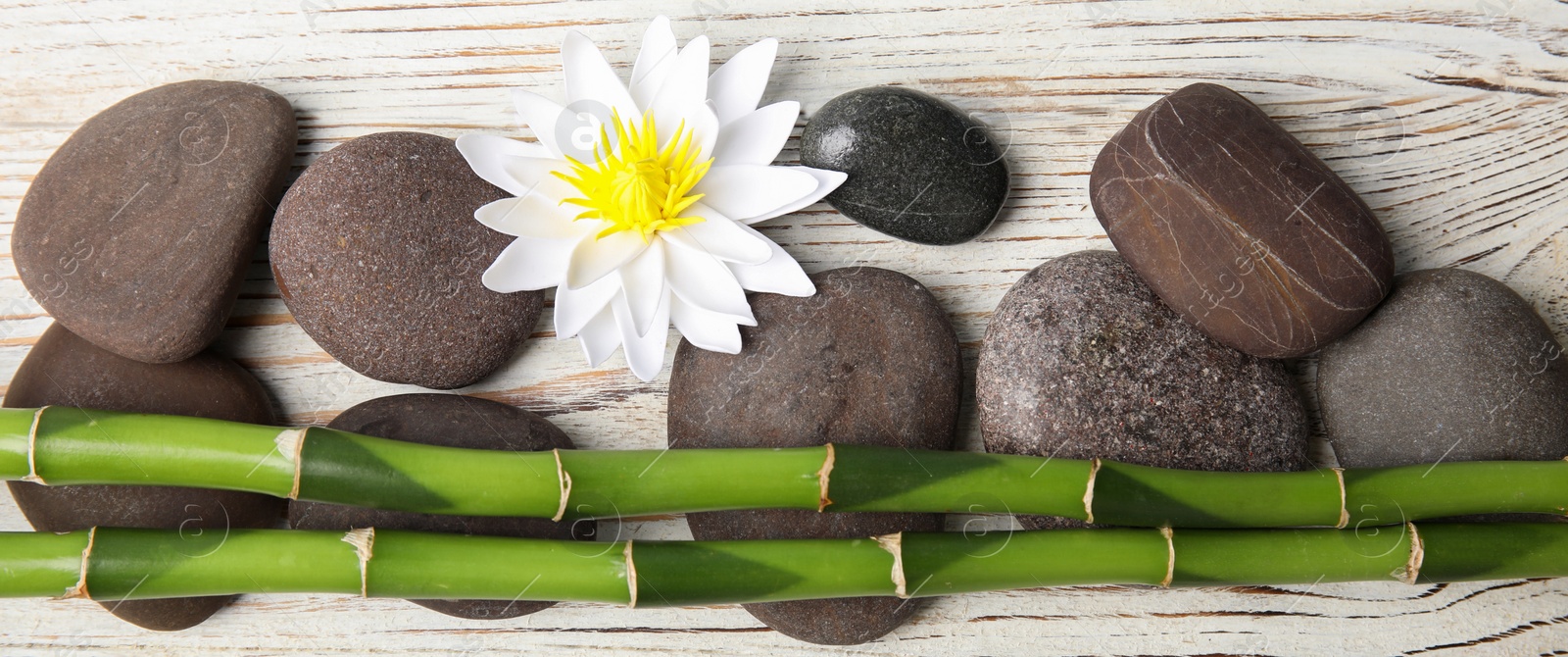 Image of Spa treatment. Flat lay composition with stones, bamboo and lotus flower on white wooden table. Banner design