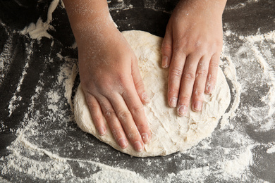 Photo of Woman kneading dough for pizza at grey table, closeup