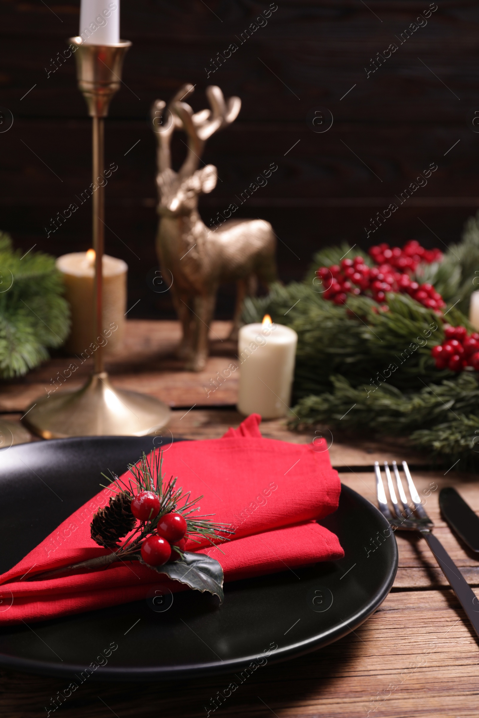 Photo of Plate with red fabric napkin, cutlery and festive decor on wooden table