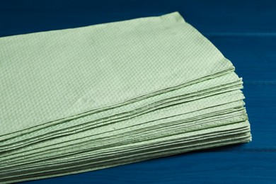 Stack of green paper towels on blue wooden table, closeup