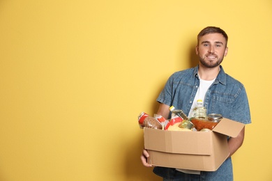 Photo of Young man holding box with donations on color background. Space for text