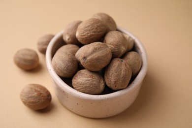 Photo of Whole nutmegs in bowl on light brown background, closeup