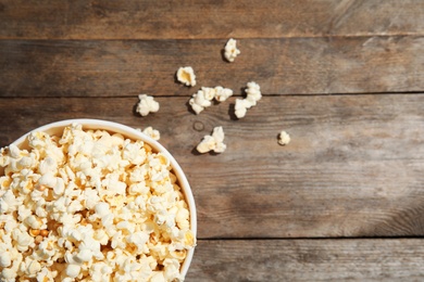 Photo of Cup of fresh tasty popcorn on wooden background, top view with space for text. Cinema snack