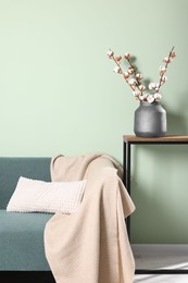 Branches with white fluffy cotton flowers on console table in cozy room. Interior design