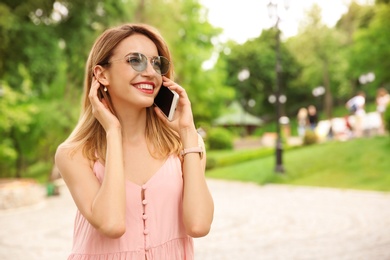 Photo of Young woman in stylish outfit talking on phone outdoors