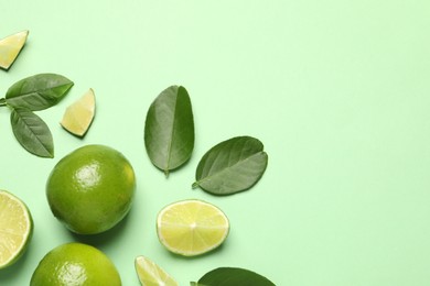 Whole and cut fresh ripe limes with leaves on light green background, flat lay