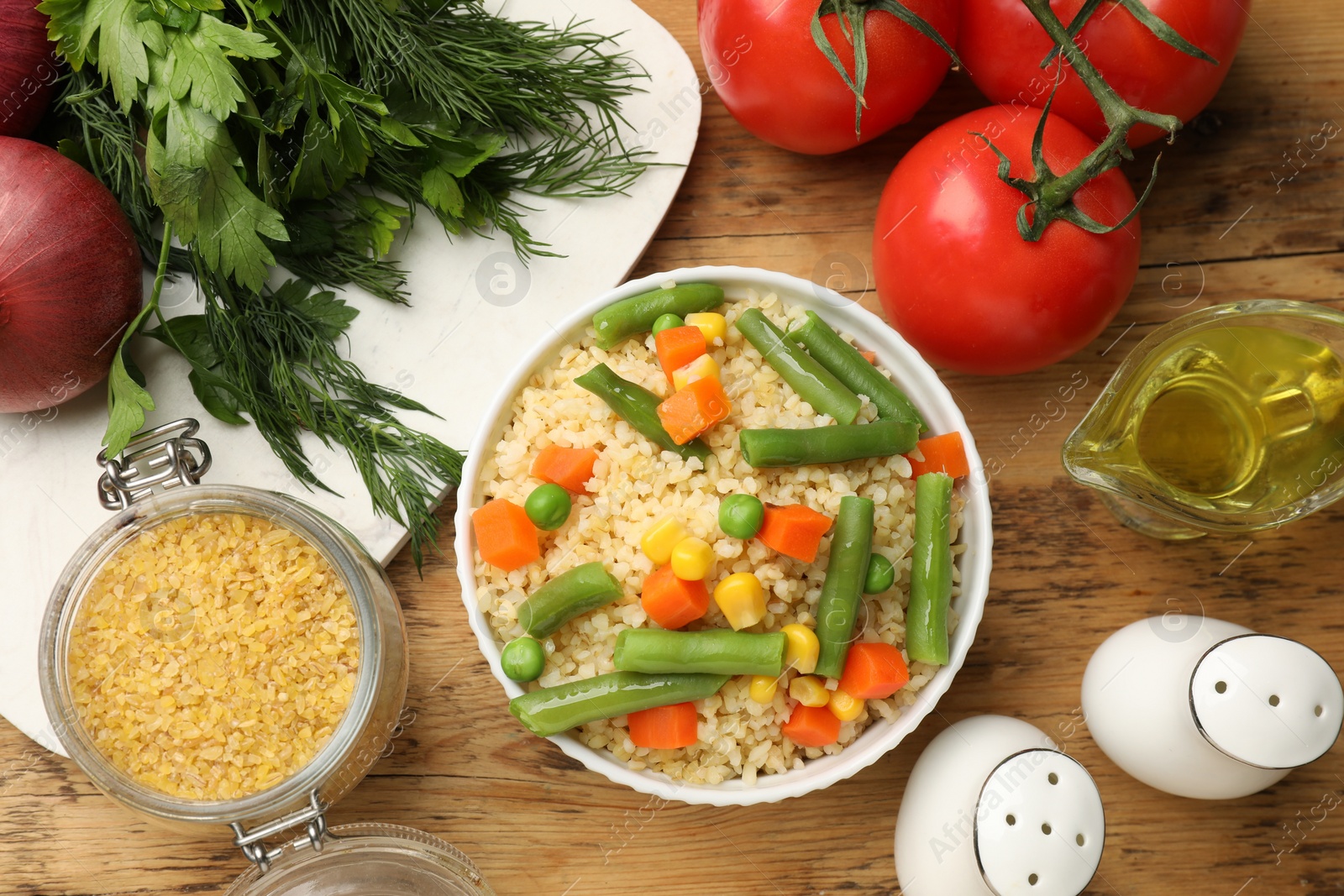 Photo of Delicious bulgur with vegetables and other products on wooden table, flat lay