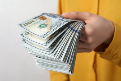 Photo of Woman holding many dollar banknotes on light background, closeup