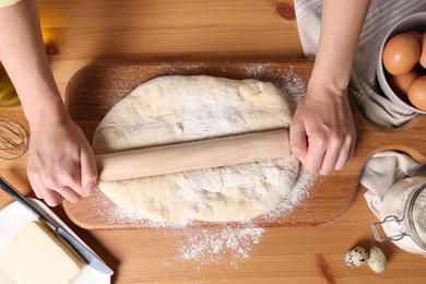 Photo of Woman rolling dough with wooden pin at table, top view