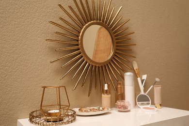 Photo of Stylish round mirror on wall over dressing table with makeup products