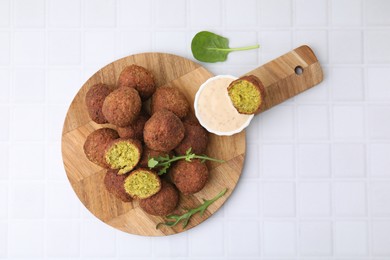 Photo of Delicious falafel balls, herbs and sauce on white tiled table, top view