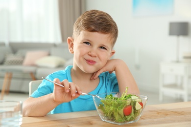 Photo of Adorable little boy eating vegetable salad at table in room