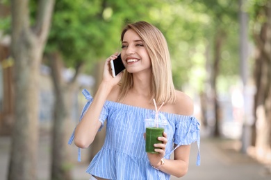 Photo of Young woman with plastic cup of healthy smoothie outdoors