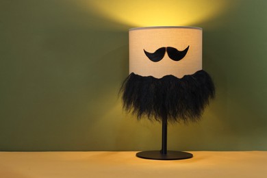 Photo of Man's face made of artificial mustache, beard and lamp on khaki background. Space for text