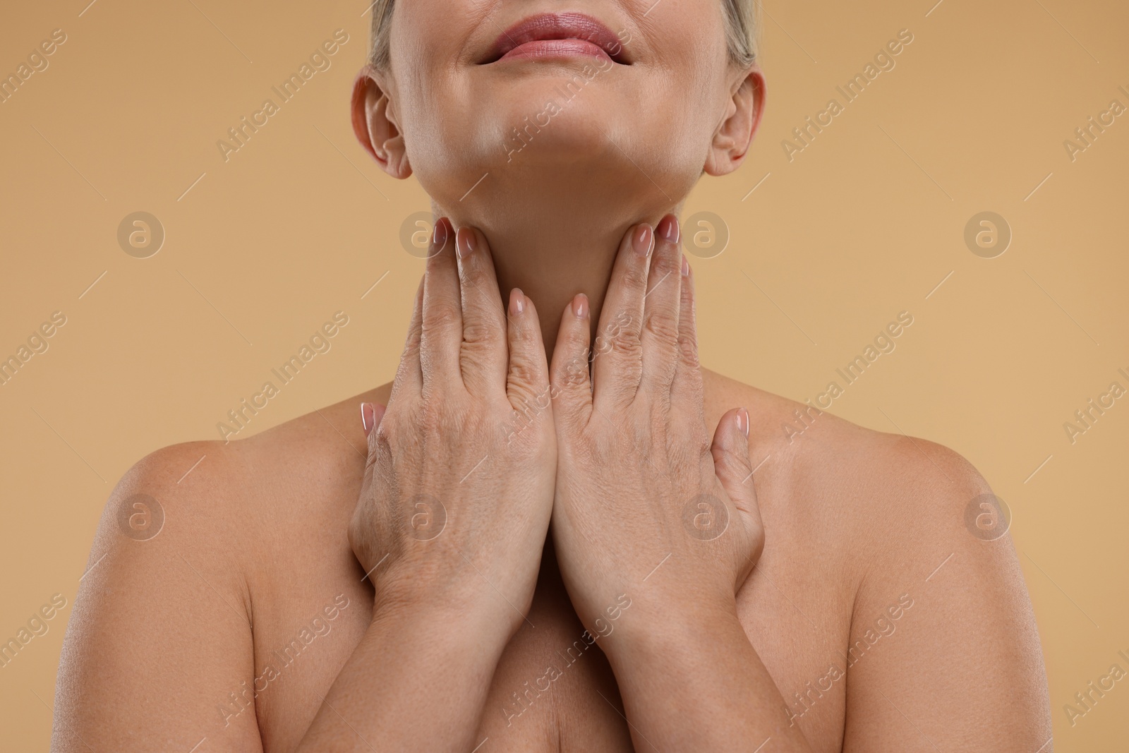 Photo of Mature woman touching her neck on beige background, closeup